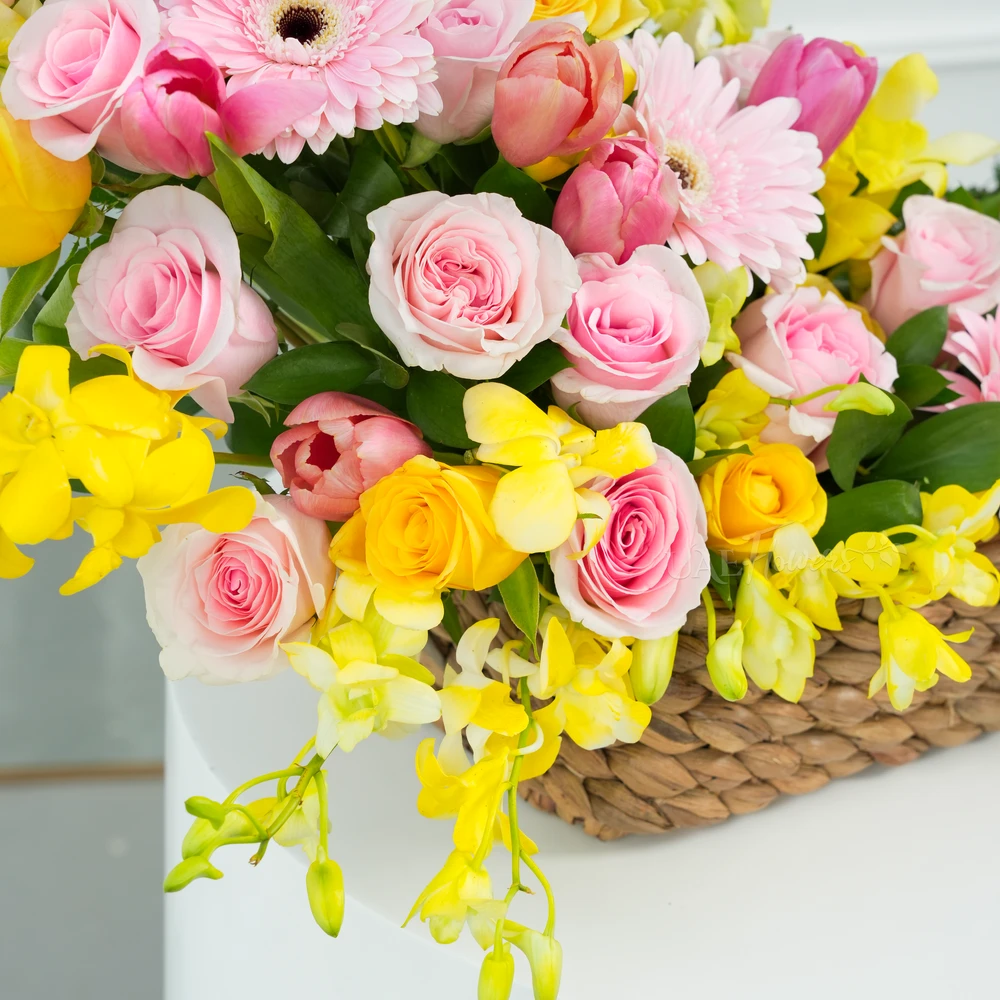 A basket arrangement of 3 pink gerberas, 15 pink roses, 5 yellow roses, 10 pink tulips and 5 stems of yellow orchids with green fillers and multi-colored easter eggs.