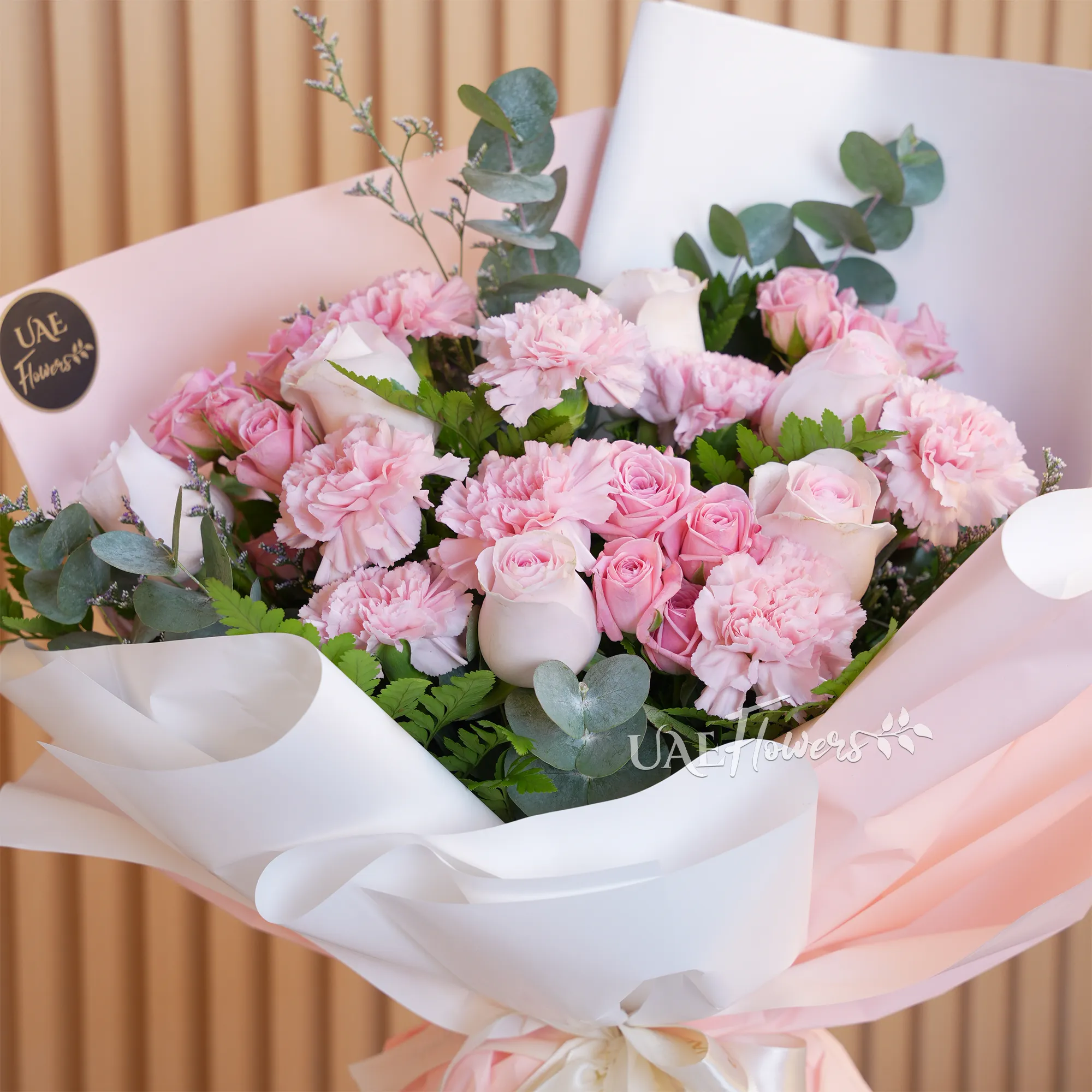 bouquet with 5 pink roses, 7 carnations, and 4 pink spray roses. Wrapped in paper with ribbons and green fillers.