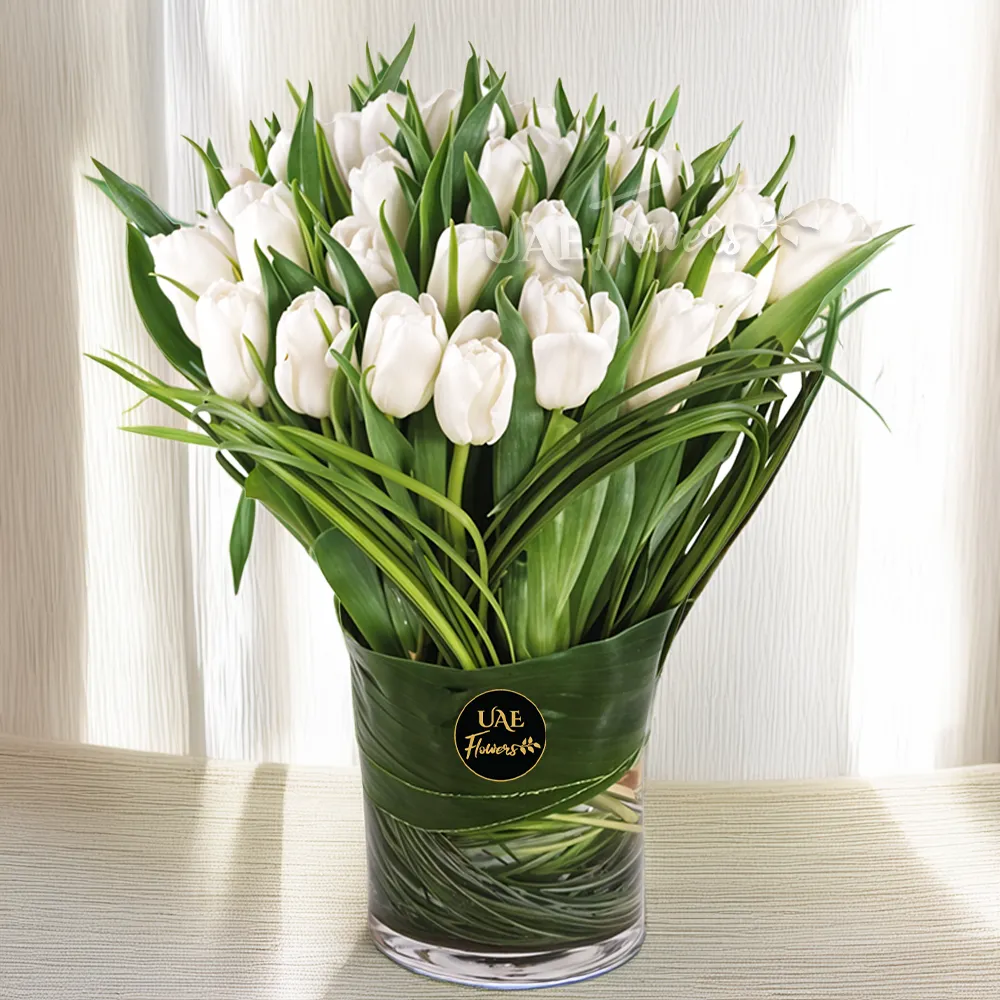 Glass vase with 30 white tulips and steel grass, elegantly arranged to symbolize purity, grace, and serenity, perfect for gifting or decor.