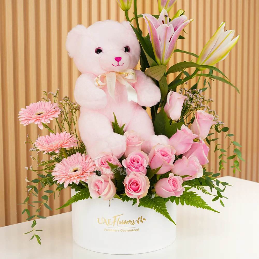 pink lily, pink gerberas, and pink roses in a round white box with a small pink teddy bear