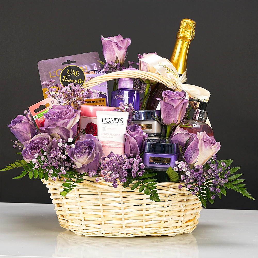 gift basket with L'Oreal skincare, candle, snacks, lipcare, and purple-sprayed white roses in a handled basket