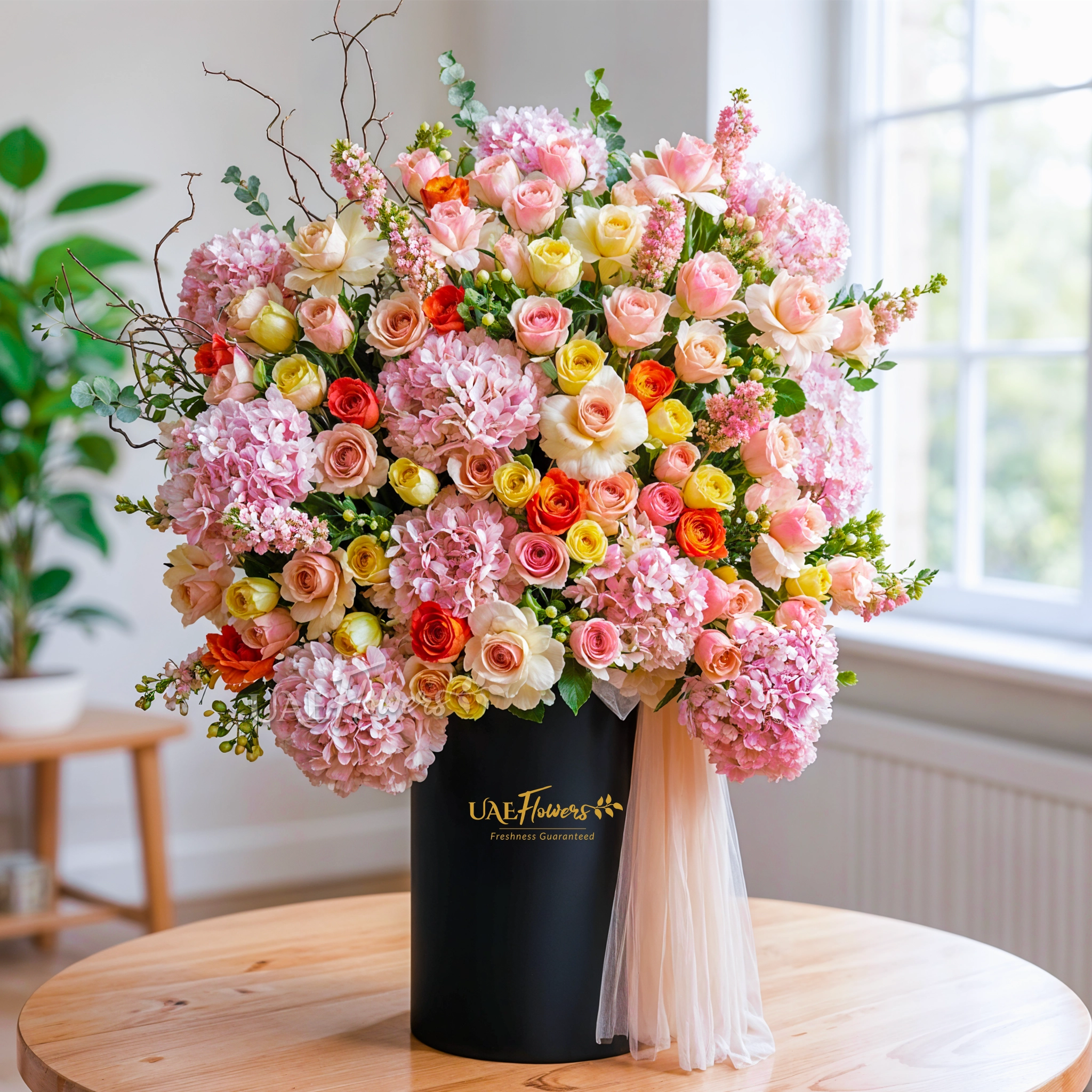 An arrangement of pink hydrangeas, pink roses, peach roses, orange roses, peach matthiola and white berries with green filler and peach net in a tall round box.